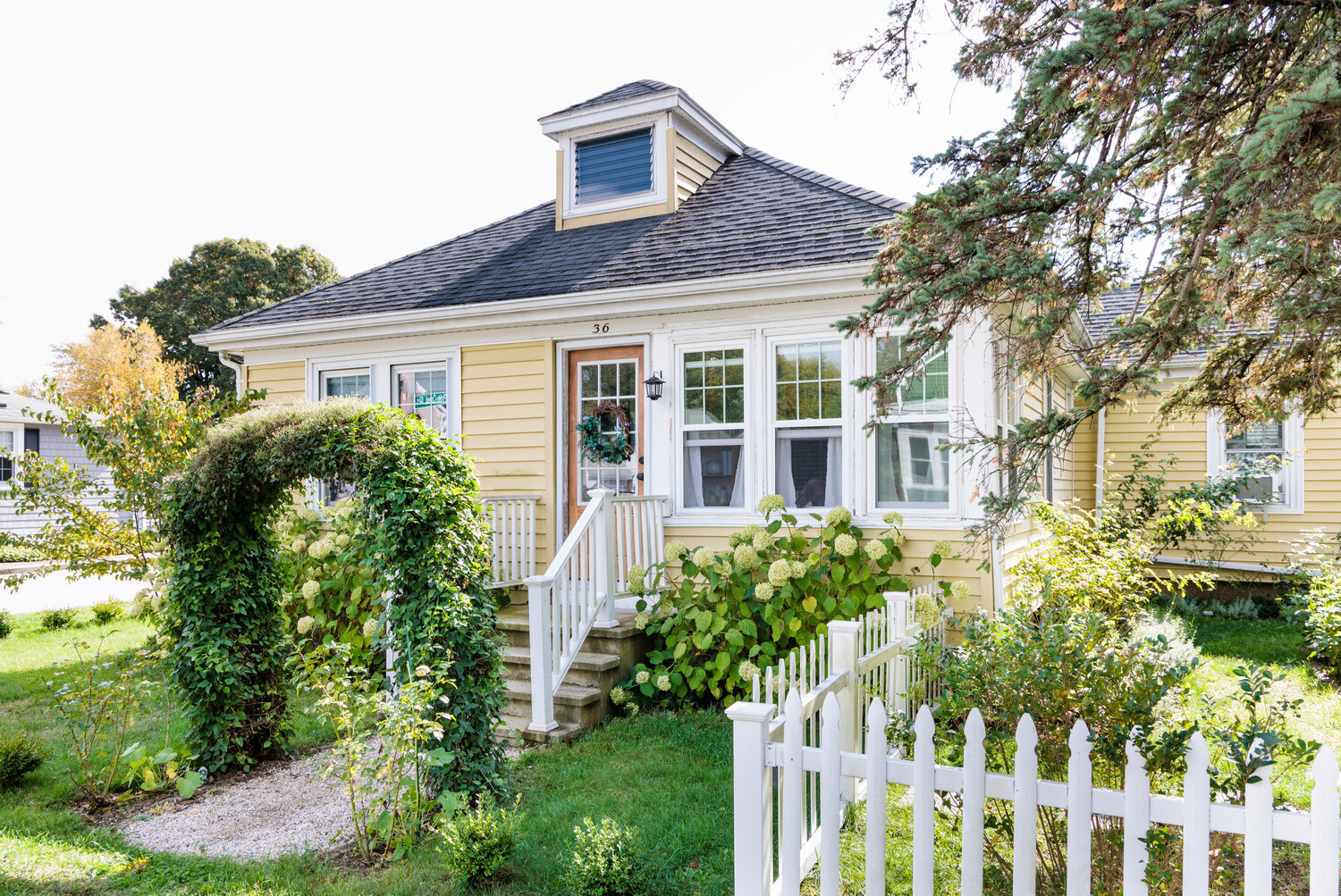 With its picket fence, vine-draped arbor, and blooming shrubs, the little 1928 cottage offers plenty of curb appeal