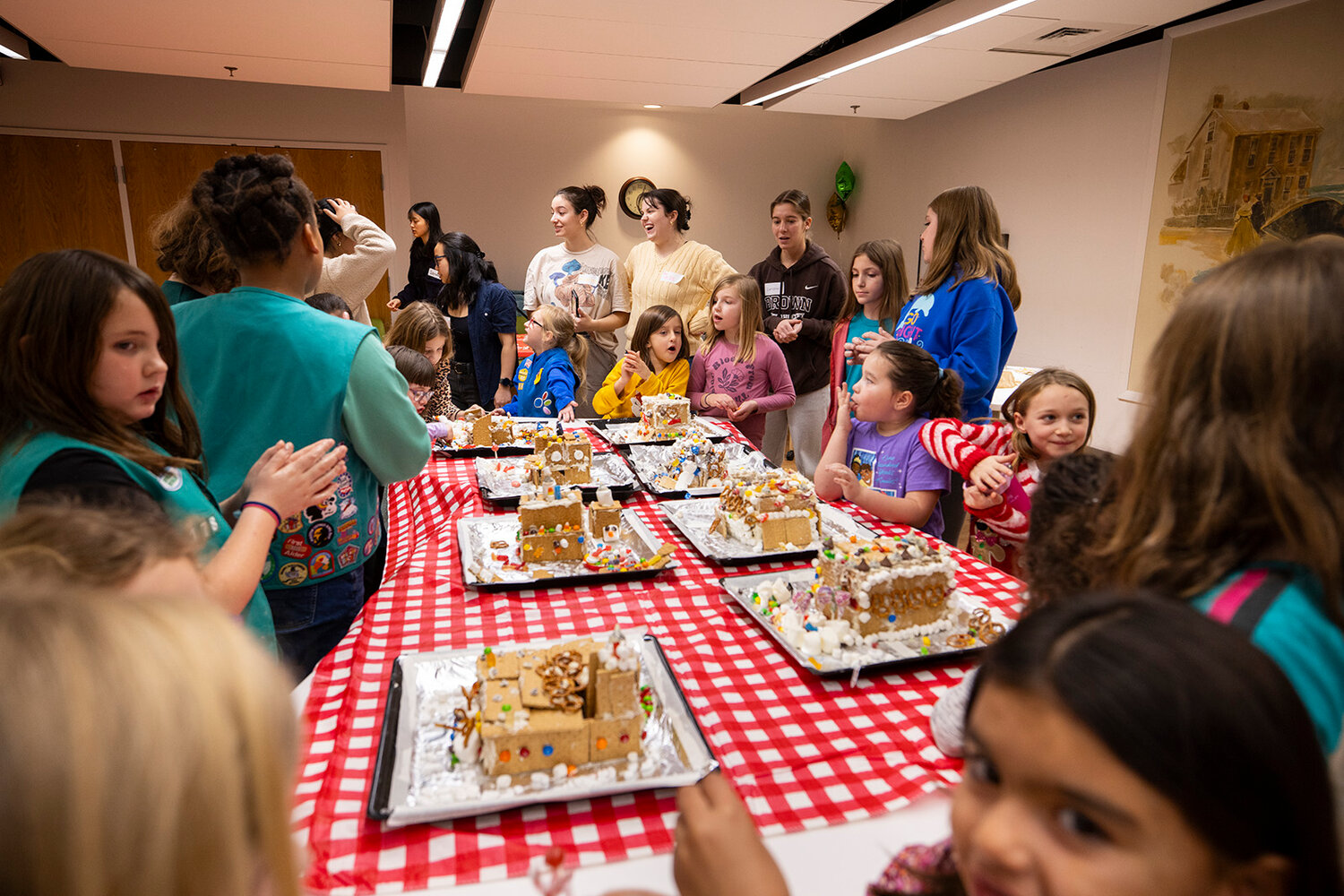 Photos of Brown University Society of Women Engineers members working with Girls Scouts at the Girl Scouts of Southeastern New England Council Headquarters in teams to build a gingerbread house that can withstand a shake test.